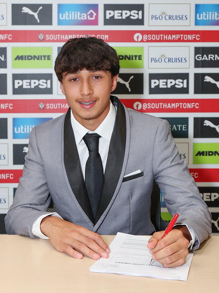 Harris Afzal smiles at the camera while signing the contract in front of him with his left hand.