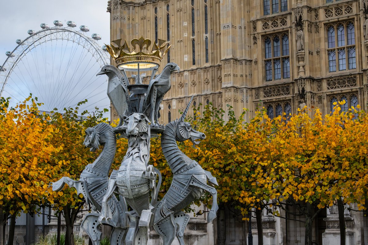 A statue of three horses in New Palace Yard, in the Palace of Westminster with autumnal brown leaves in the background