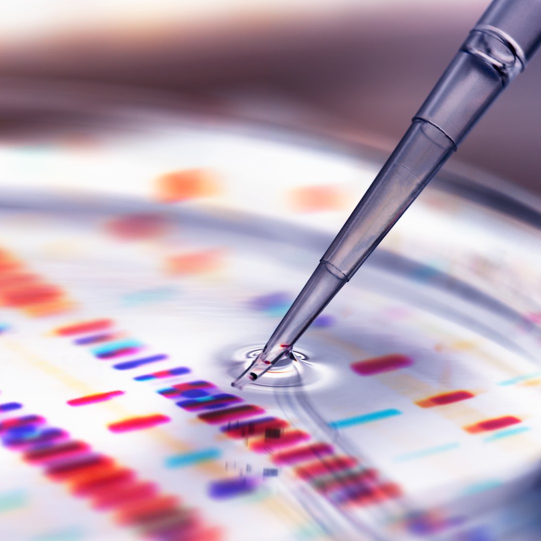 A pipette tip dips into clear liquid within a petri dish. Colorful DNA bands are visible below the surface in the background.