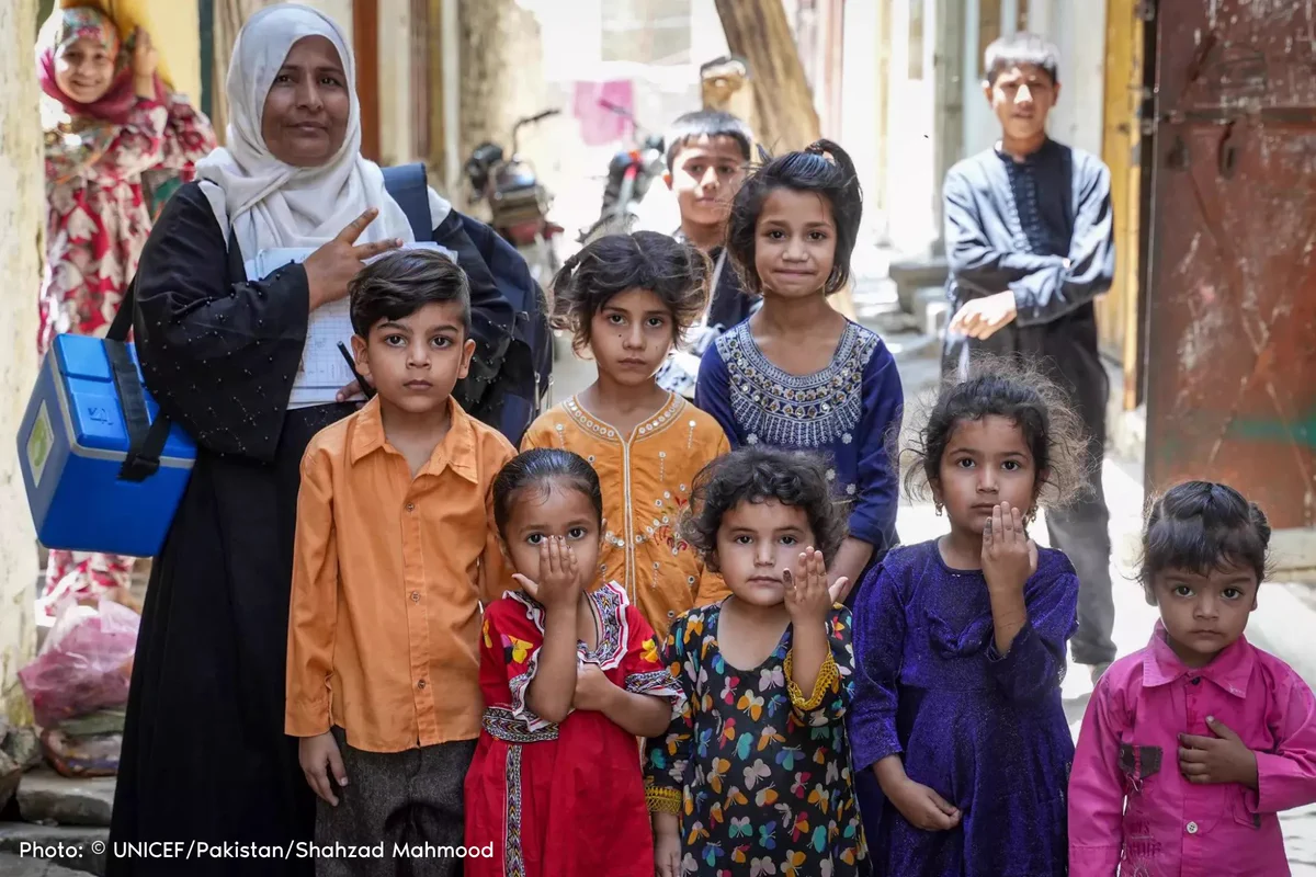 A UNICEF community mobilizer stands with a group of children showing off their purple tipped fingers indicating they have been vaccinated against polio.