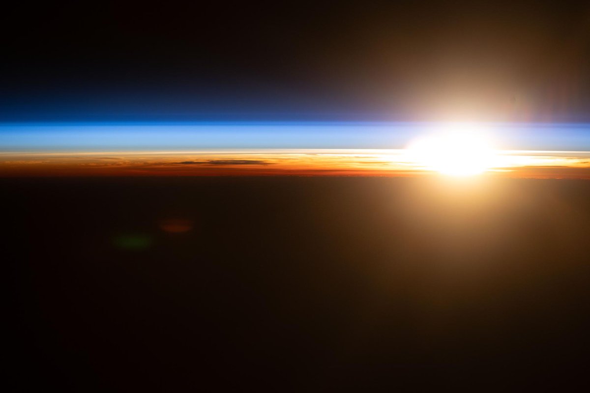 An orbital sunrise above the Pacific Ocean illuminates Earth’s atmosphere, revealing cloud tops and orange and blue hues outlining the planet’s horizon.
NASA/Jessica Meir