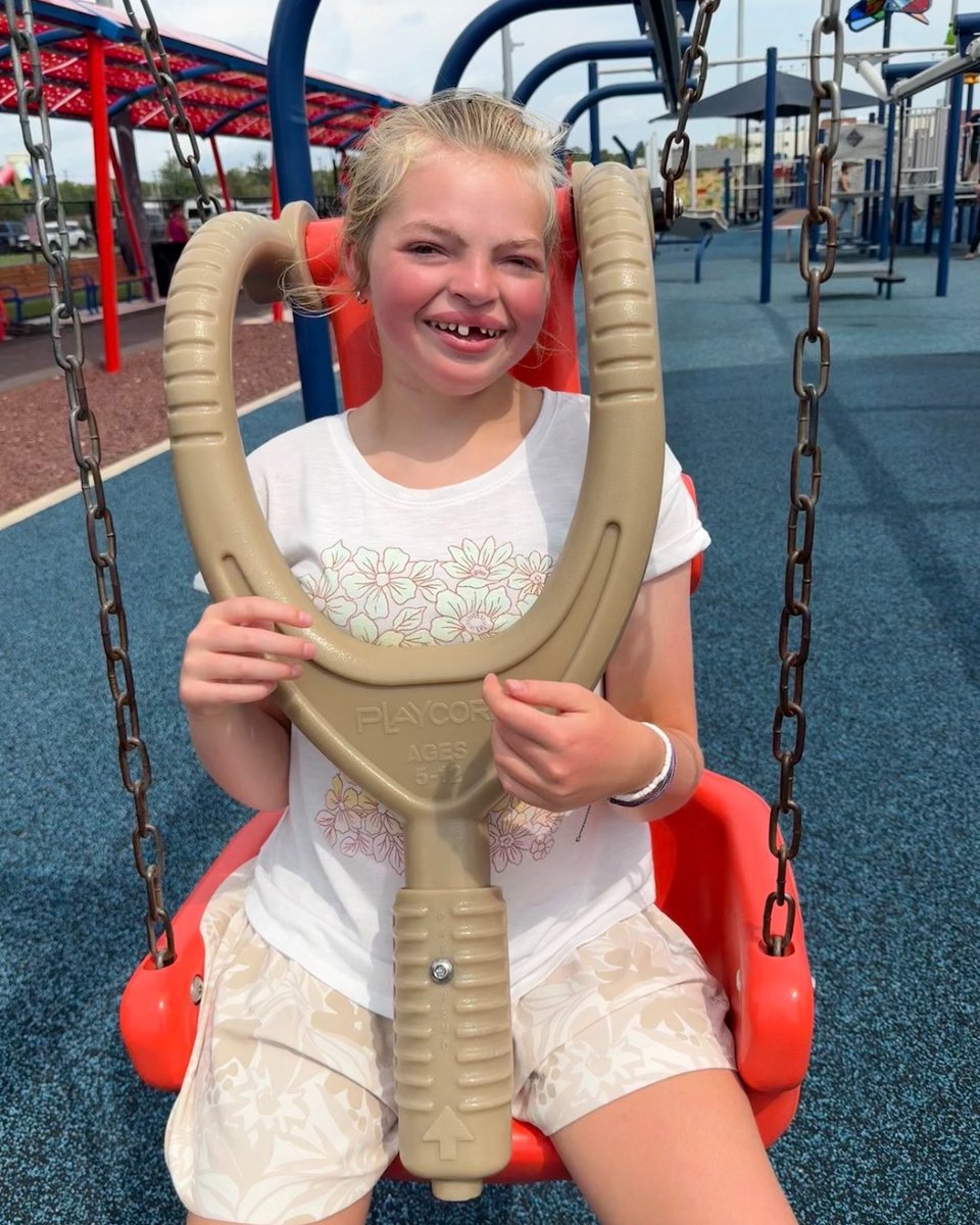 Quinn smiling in a swing at an accessible playground