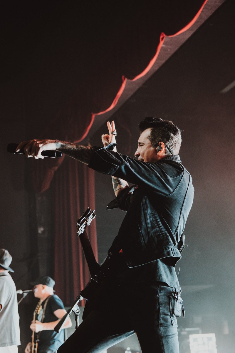 Musician with a guitar on stage holding a microphone and making a gesture.