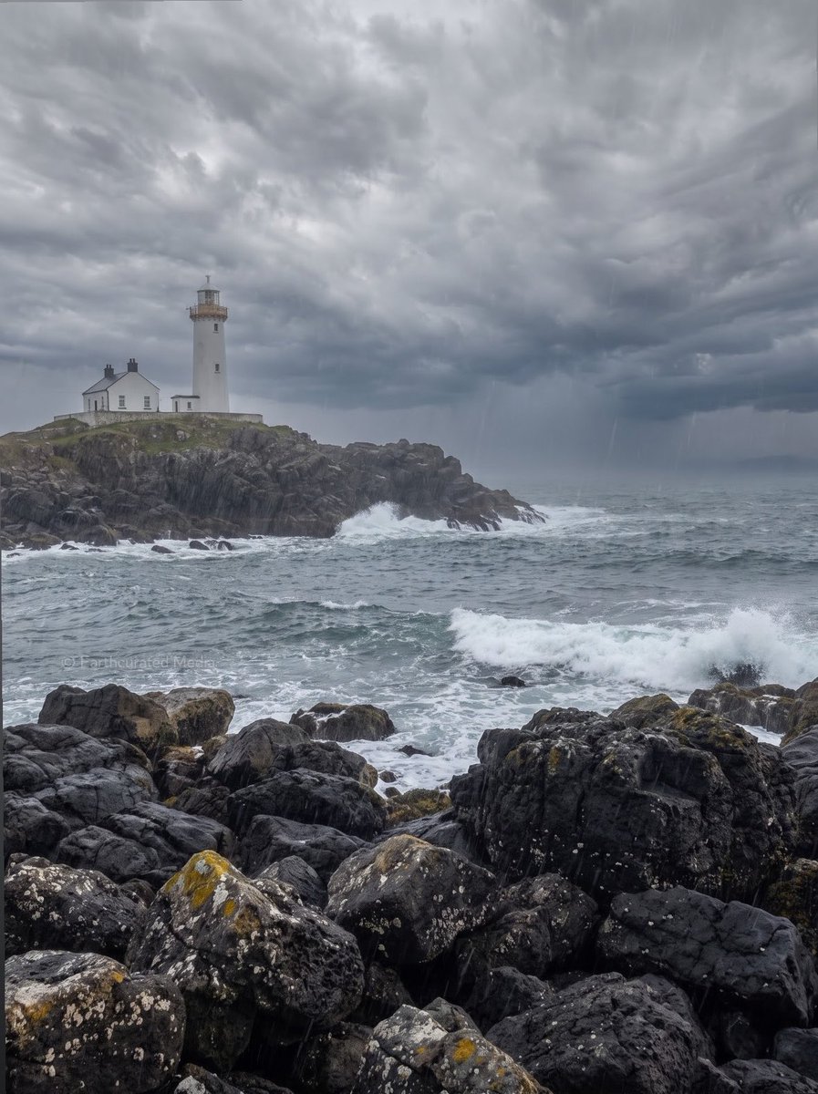 Two original Earth Curated images showing the same white lighthouse and rocky coastline from the same viewpoint in contrasting weather one beneath clear blue skies and calm seas, the other during heavy rain with dark storm clouds and rough water. Visuals produced by @earthcurated.