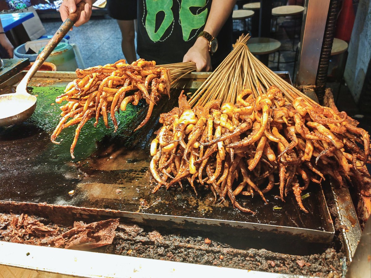 1Baddestbitch's tweet photo. Tasty street food alert! Crispy fried squid skewers with spicy seasoning—perfect snack for a walk at dusk. ， https://t.co/j5pWsSXJJJ