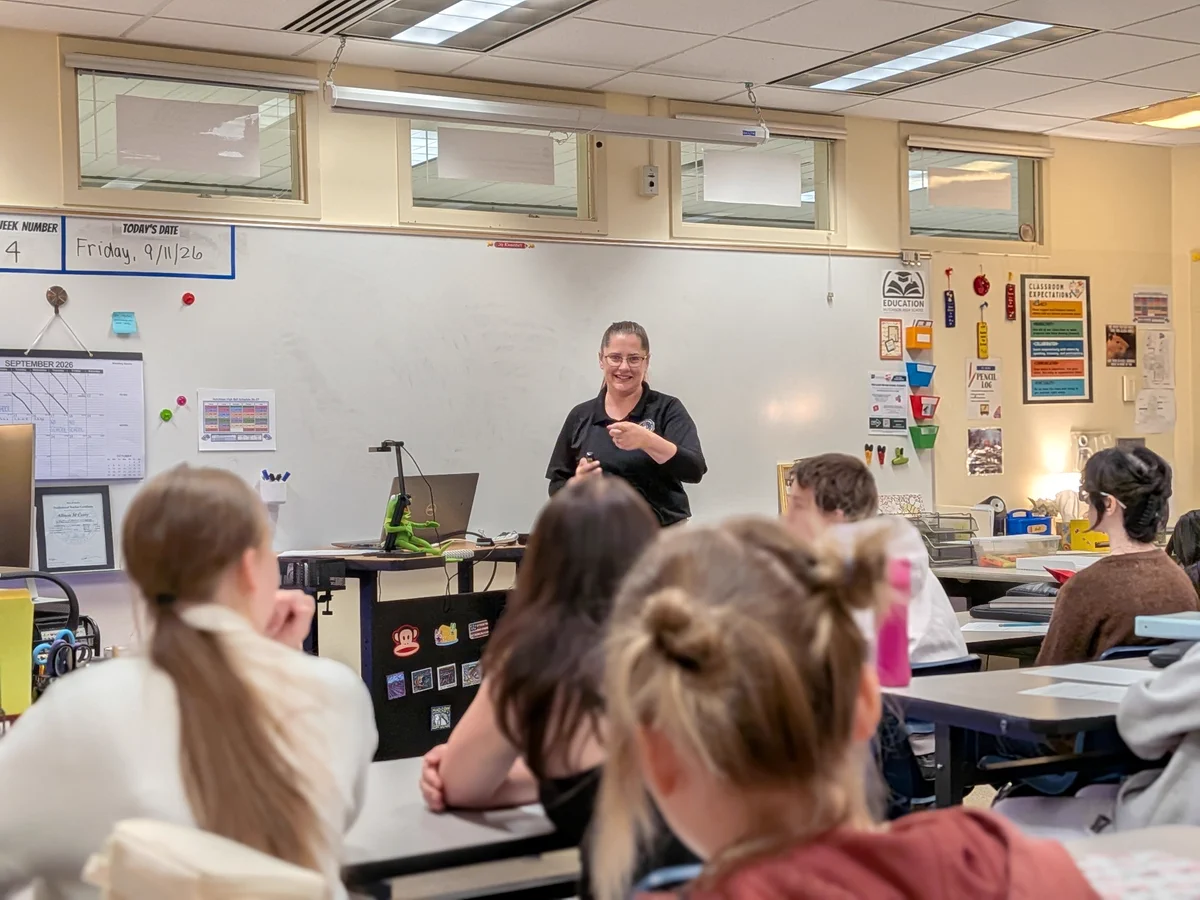 An FBI employee standing at the front of a classroom interacting with students seated at desks.