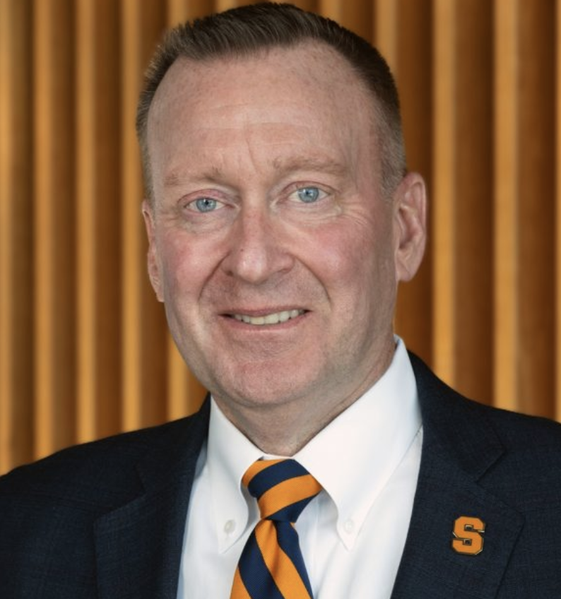 photo of person looking direclty into camera lens. He is wearing the traditional colors and logos representing Syracuse University