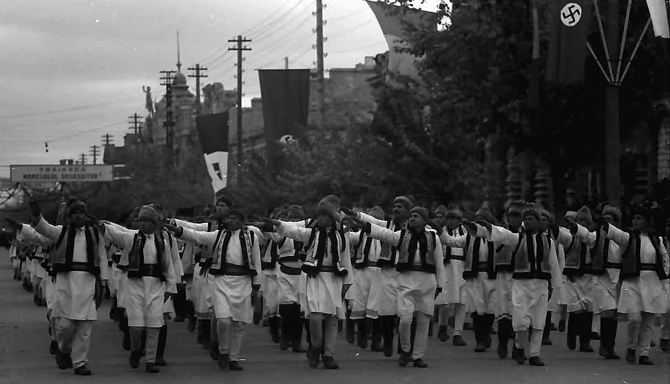 GHarward's tweet photo. Romanian men in traditional peasant attire give a fascist salute under the flags of Romania, Nazi Germany, &amp; Fascist Italy during a parade in Chişinău in 1942. https://t.co/VU5g9eafEq