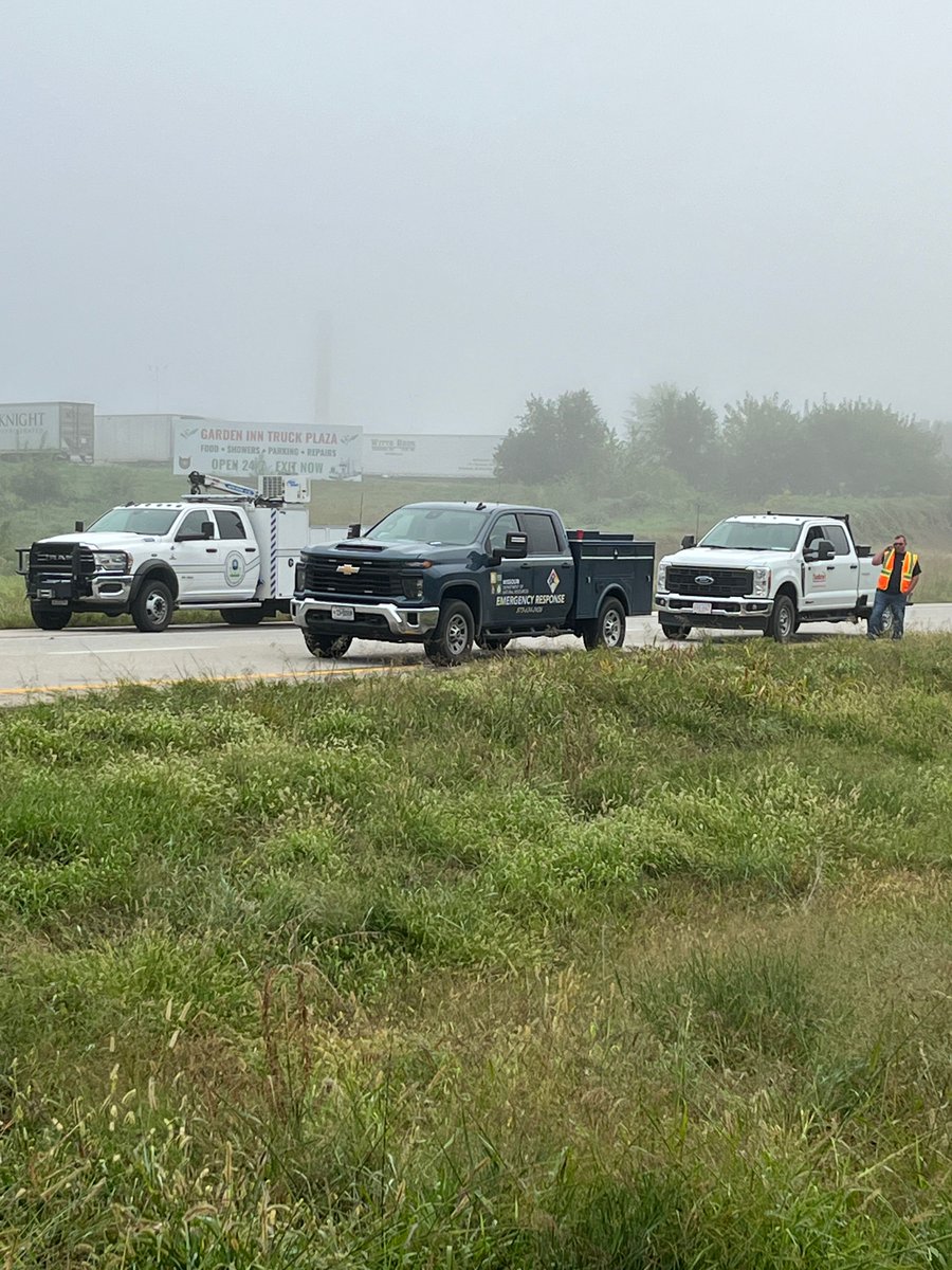 Three pickup trucks parked on a foggy roadside with a worker in a safety vest standing nearby.