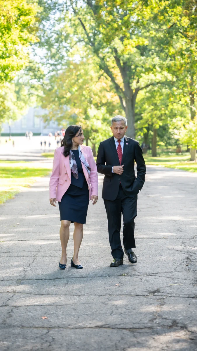 Minister Anand and Minister Balakrishnan walking through the gardens of Rideau Hall, with trees in the background.