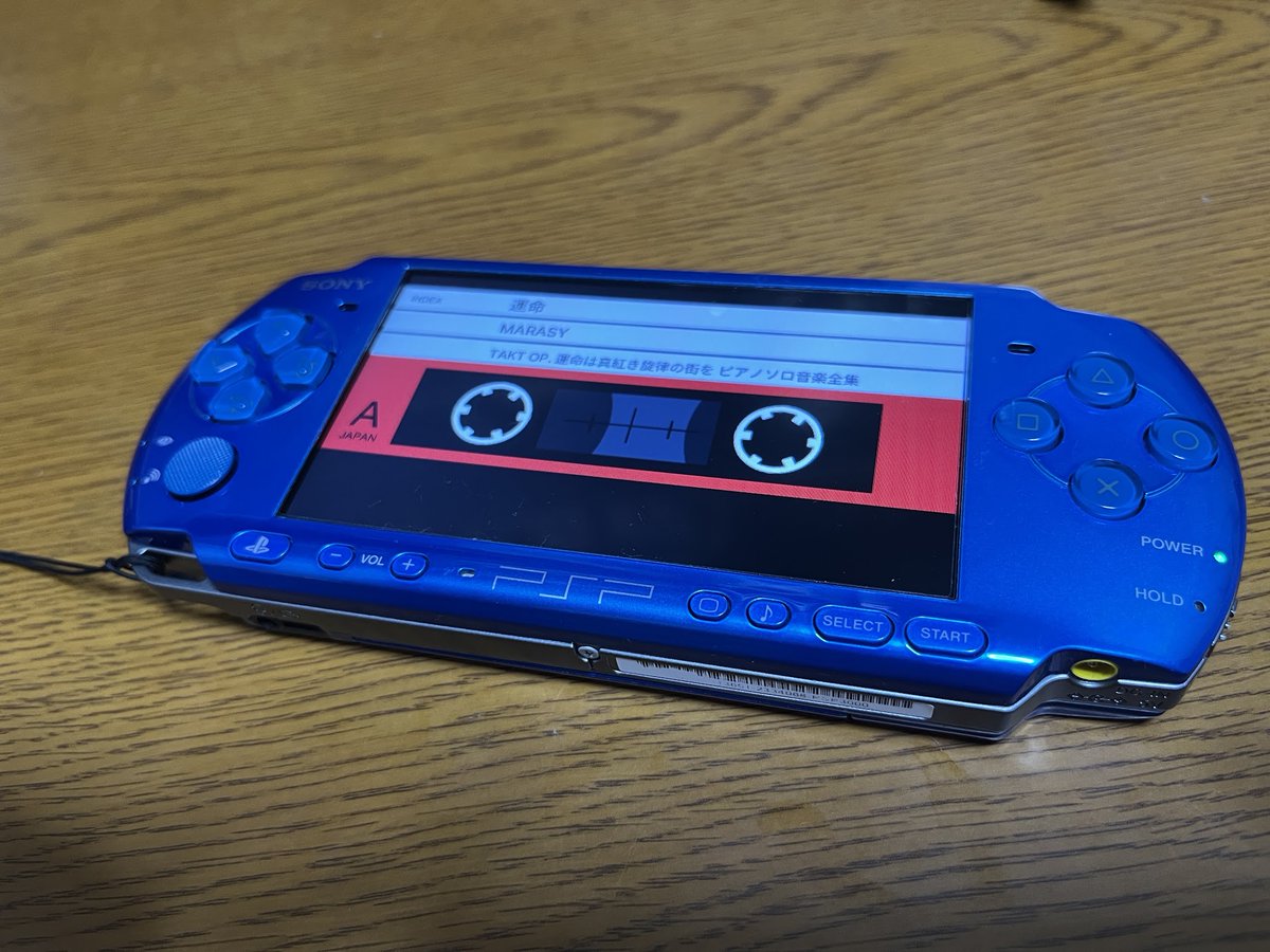 Blue Sony PSP displaying PSPMAN's cassette view, on a desk