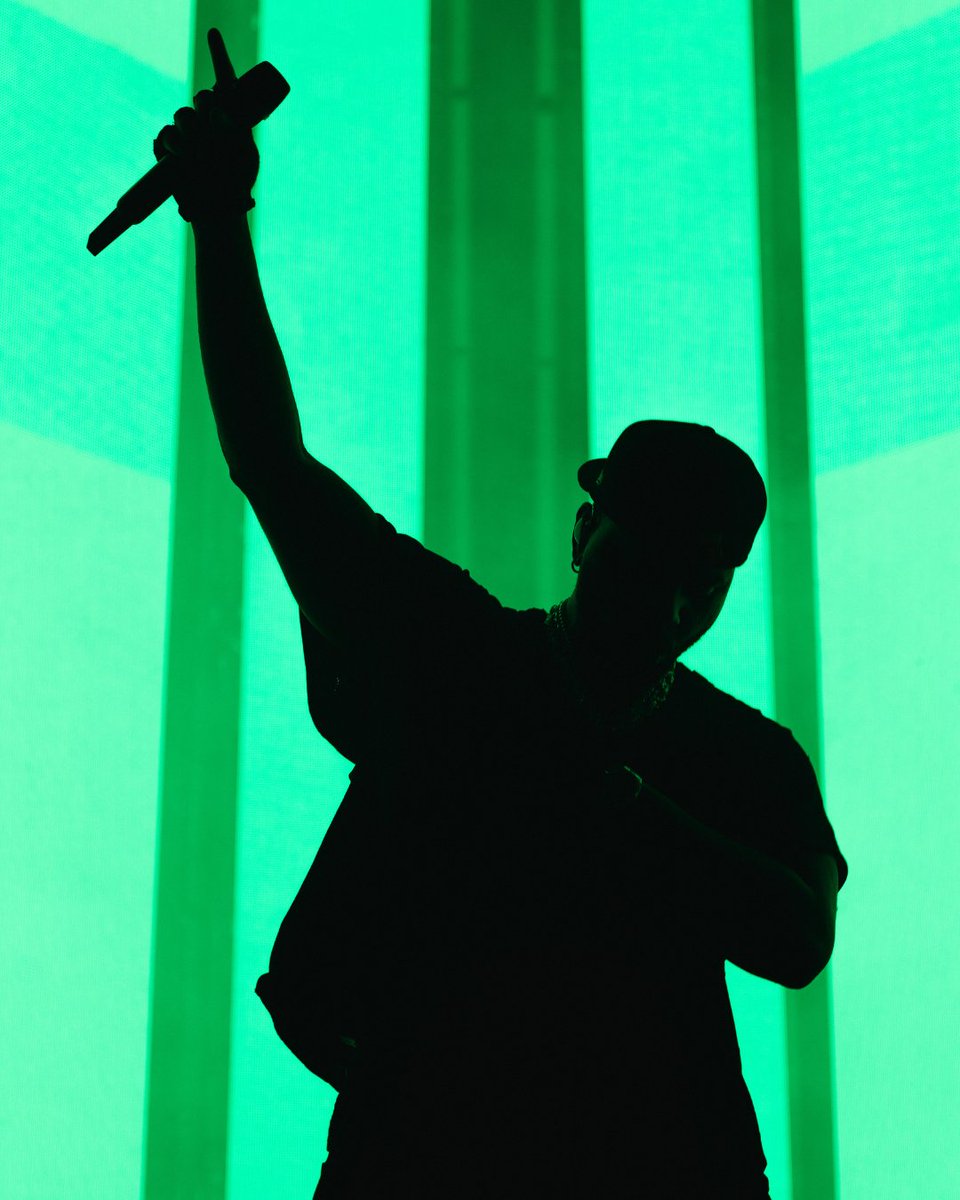 A silhouette of a person holding a microphone on stage against a bright green background.