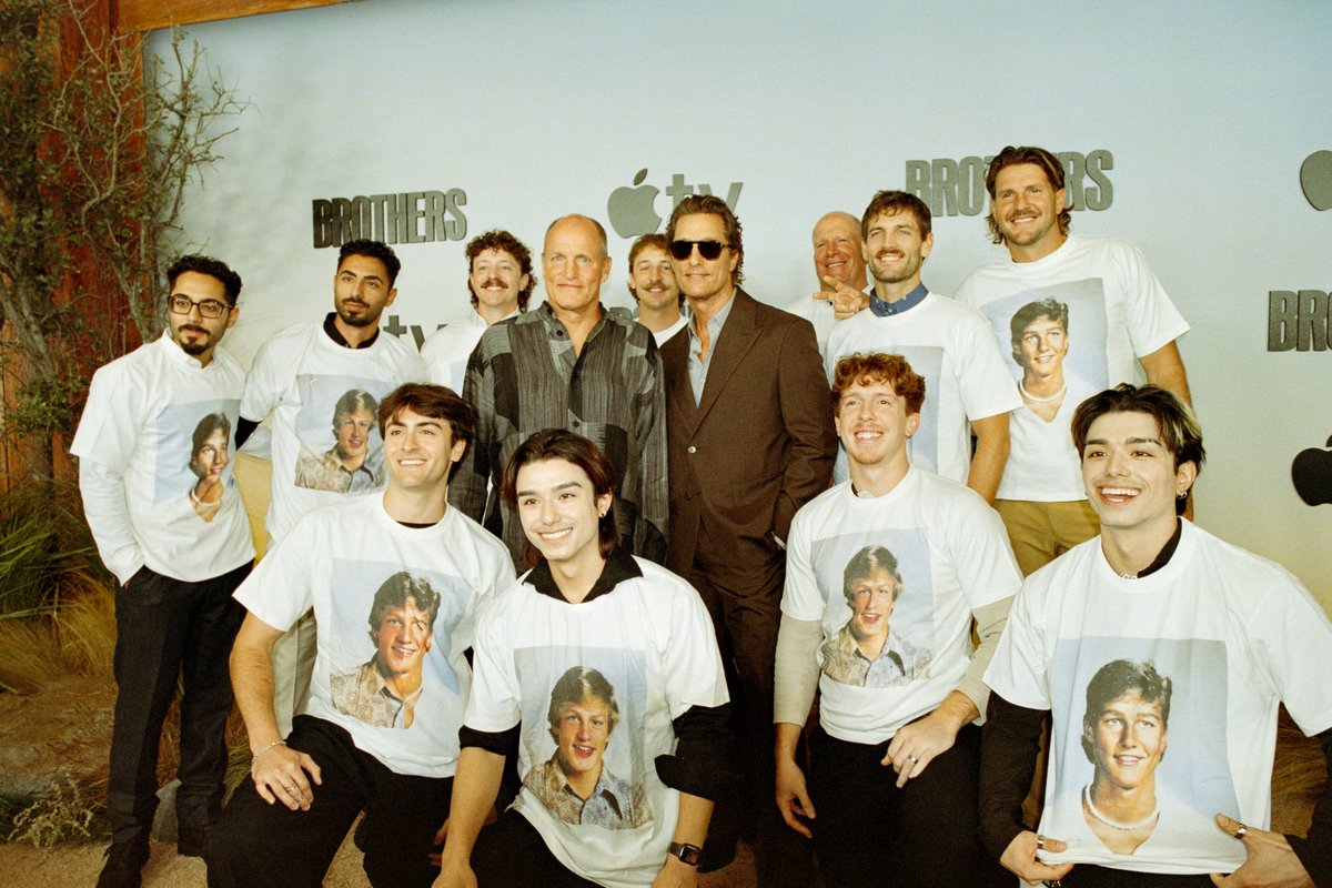 From the premiere of Brothers. Matthew McConaughey and Woody Harrelson pose with a group of creators. The creators are all wearing white shirts that feature a younger Matthew or a younger Woody on them.