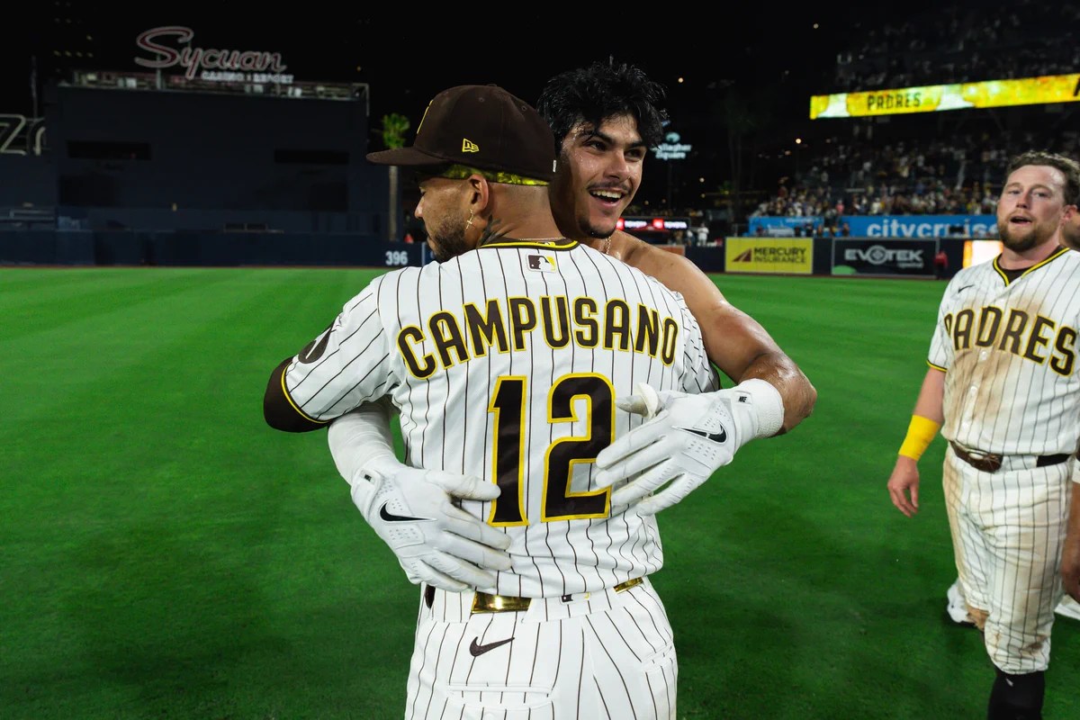 Ethan Salas and Luis Campusano hugging. They are wearing the Padres home white pinstripe uniform.