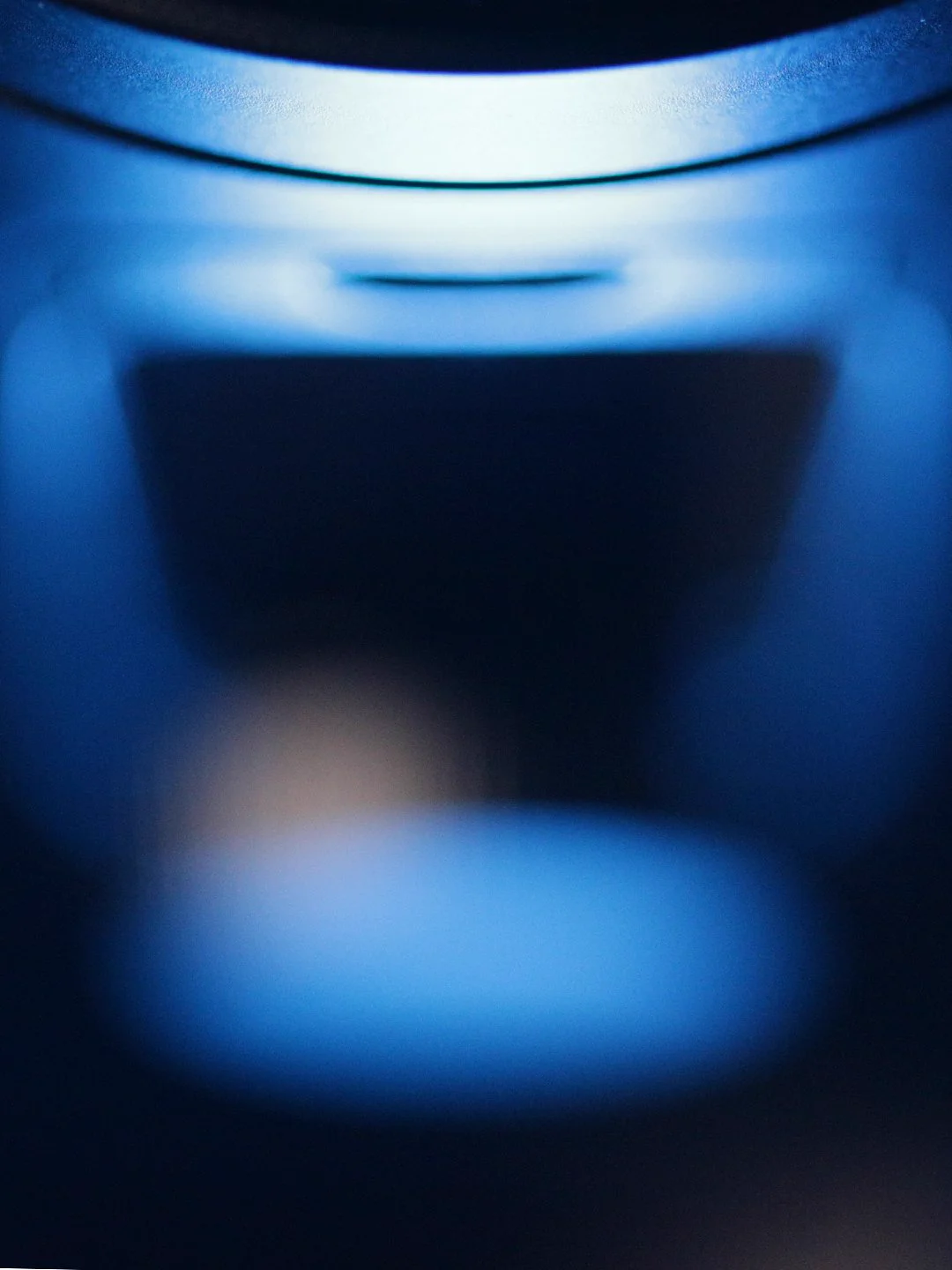 A closeup, blurred photo of a premium piece of hardware, top-lit with a dramatic blue light that creates dark shadows.