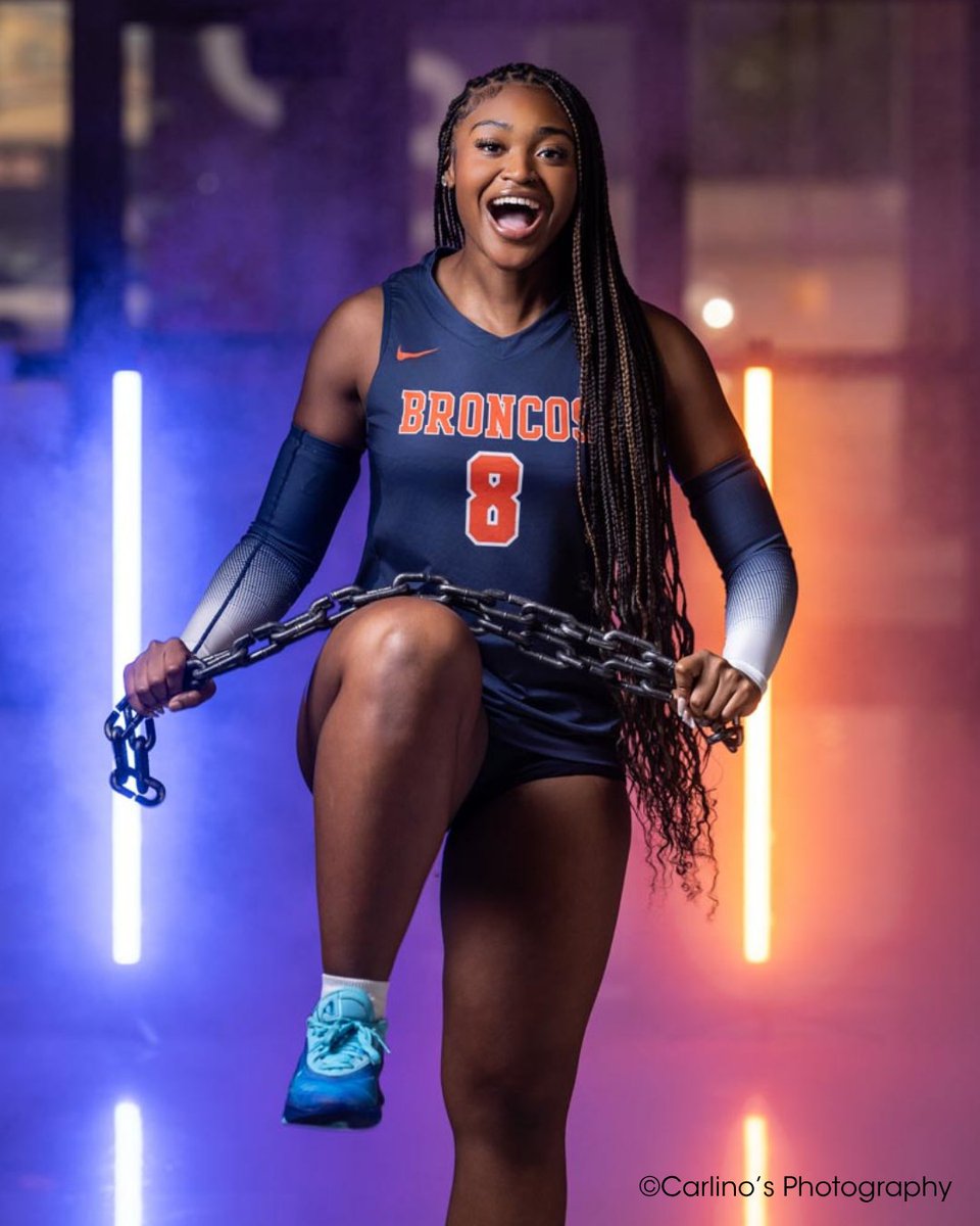 An athlete in a "Broncos" uniform, with number 8, poses confidently while holding a chain and raising one leg. The background features vivid blue and orange lights. Copyright Carlino’s Photography.