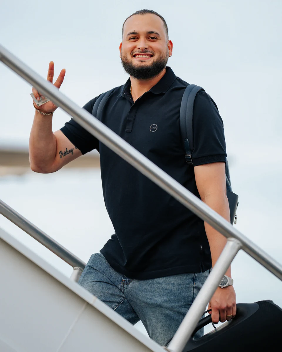 Juan Morillo holds up a peace sign and smiles at the camera as he walks up the steps to board the plane.