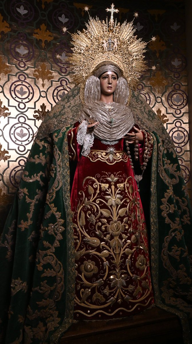 pasoyesperanza's tweet photo. “𝐕𝐢𝐭𝐚, 𝐝𝐮𝐥𝐜𝐞𝐝𝐨 𝐞𝐭 𝐬𝐩𝐞𝐬 𝐧𝐨𝐬𝐭𝐫𝐚, 𝐬𝐚𝐥𝐯𝐞”

María Santísima de la Esperanza, ataviada para el mes del Rosario.

La festividad del Santo Rosario -a conmemorar el próximo 7 de octubre- guarda una íntima vinculación con la Orden de Santo Domingo -y, por tanto, con nuestra parroquia-, al aludir a la tradición de la recepción del Rosario de manos de la Virgen por parte de Santo Domingo de Guzmán, fundador de la Orden.

Para la ocasión, Santa María de la Esperanza viste saya de terciopelo carmesí bordada en oro, siguiendo diseño de Javier Sánchez de los Reyes, tomando como punto de partida una serie de valiosas piezas bordadas del siglo XIX; ejecución por el taller de Salvador Oliver Urdiales (2021). A su vez, luce manto de terciopelo verde bordado en oro (1951-1952), confeccionado a partir del antiguo manto de procesión que bordaran las Monjas de los Ángeles Custodios y que fuese estrenado en 1944.

Las divinas sienes de la Santísima Virgen son coronadas por diadema de plata sobredorada de Orfebrería Villarreal según diseño de Juan Casielles del Nido (1971). Su rostro se enmarca por un lamé de oro francés (primer tercio del s. XX), rematando la composición la toca de sobremanto en encaje de oro (años 40 del s. XX).

En cuanto al enjoyado, destaca la presencia y rotundidad del voluminoso rosario de filigrana cordobesa en manos de la Virgen, simbolismo inherente a la festividad a conmemorar en el cercano mes de octubre. Sostiene en su mano diestra un pañuelo de encaje de Luxemburgo (finales del s. XVIII) y una azucena de oro.

Además, destaca en su pecho el clásico alfiler con la advocación de Nuestra Madre y una delicada cruz de esmeraldas, ofrenda de las camareras de la Santísima Virgen. En su vientre, la Señora luce su reconocible broche a modo de sol, ejecutado en plata sobredorada, mientras que el monograma JHS, sobre una esfera de madreperla, se compone a partir de amatistas. Sobre dicha pieza, un broche de circonitas completa el ajuar.

#CofradíasMLG
