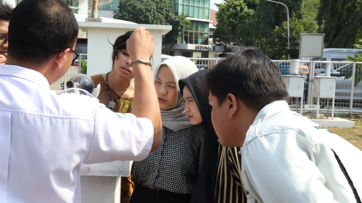 Keempat mahasiswa magang sedang mengamati sebuah alat meteorologi bebentuk bola kaca bernama campbell stokes di area luar ruangan. Di sisi kiri, seorang petugas BMKG mengenakan kemeja putih sedang memberikan penjelasan.