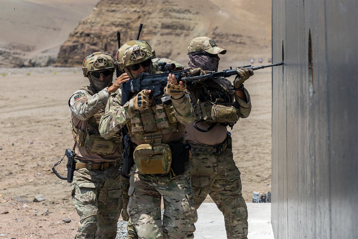 U.S. and partner service members stack along a wall with rifles during close-quarters training.