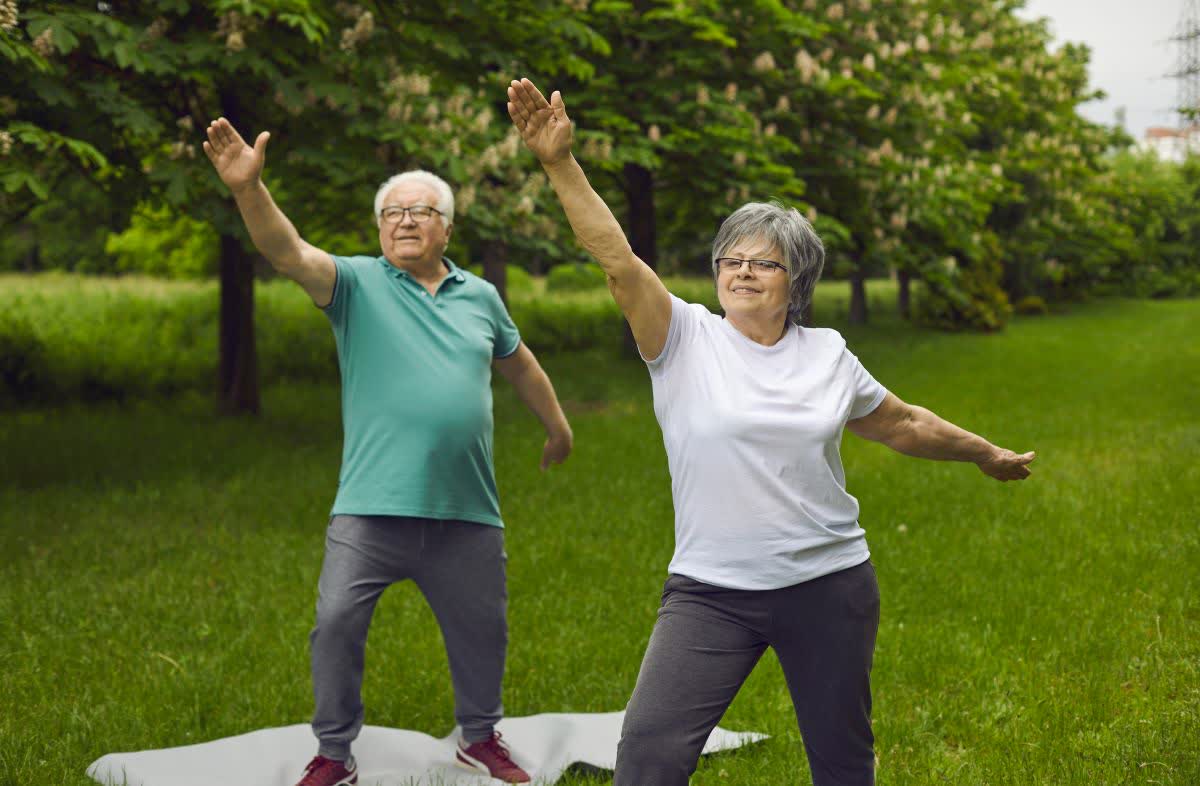 An older couple doing yoga stretches outdoors.