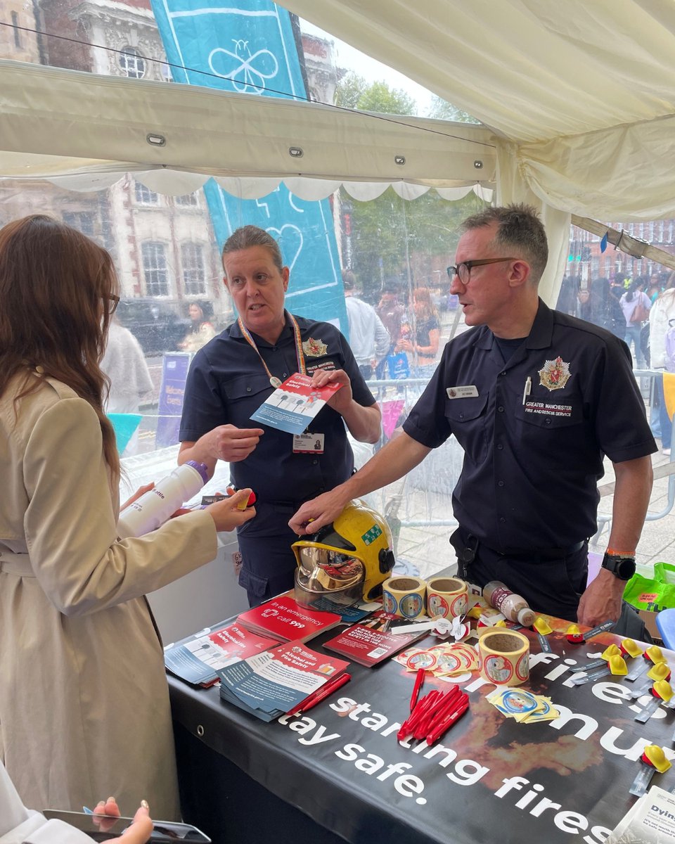 GMFRS staff members in uniform sharing leaflet with member of the public, at a stall