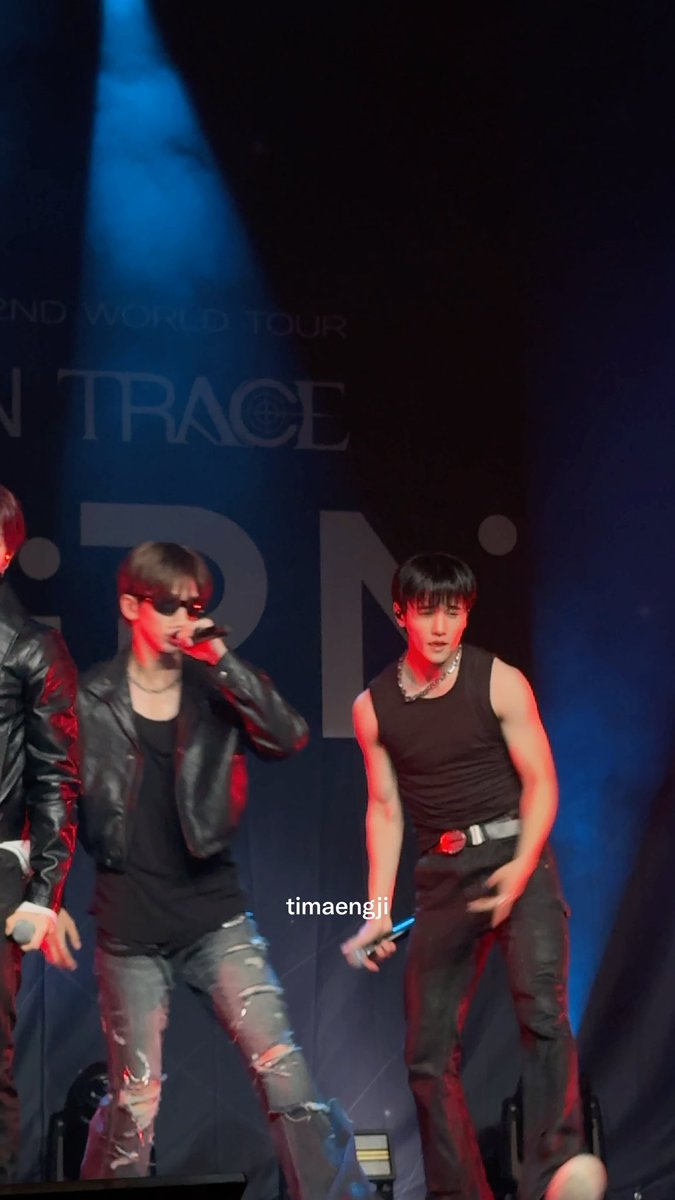 Two male performers in black outfits perform on stage under red and blue lighting, with a backdrop reading '2ND WORLD TOUR' and 'TRACE'.