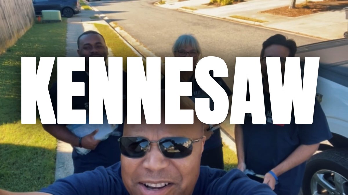 A selfie-style group photo of four people outdoors overlaid with large white text reading 'KENNESAW'.