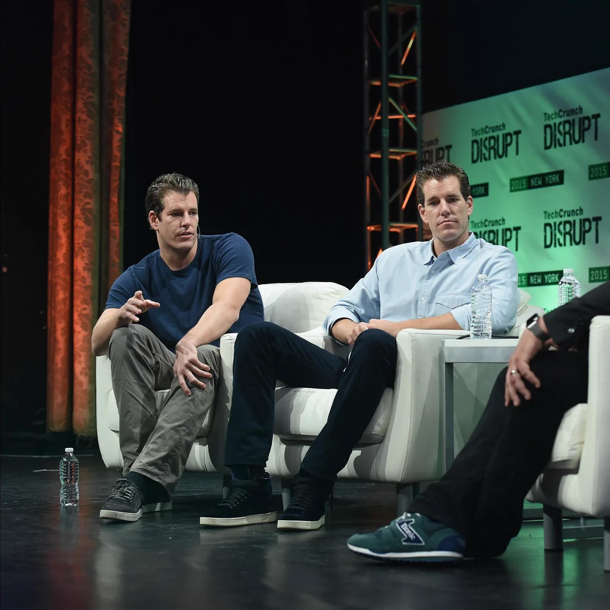 Three individuals are seated on stage during TechCrunch Disrupt in New York. They are engaged in a discussion, with two sitting on a white couch and one on a chair. The background features TechCrunch Disrupt branding.