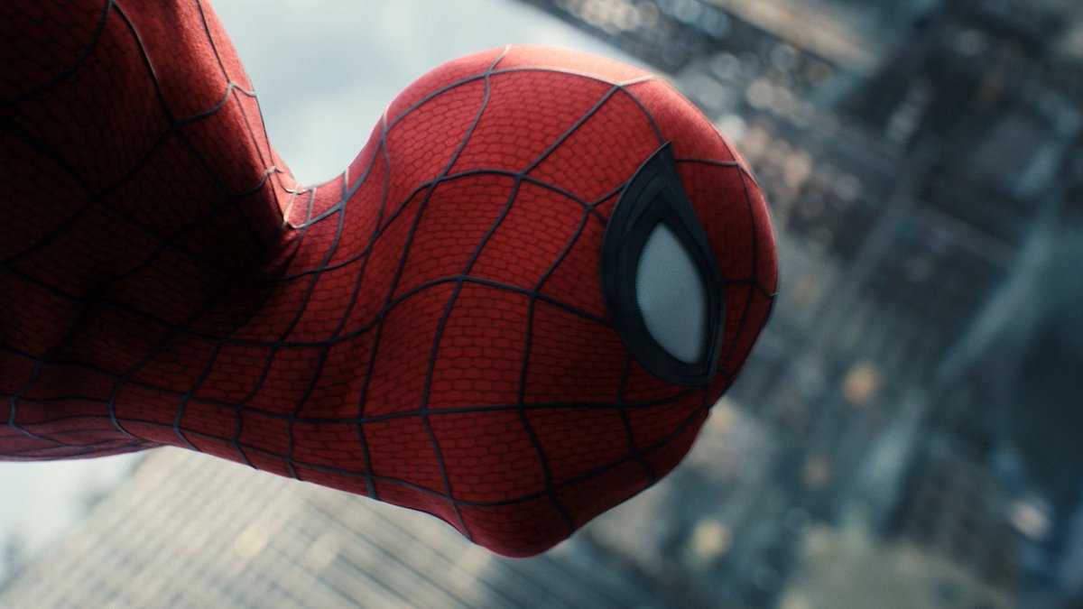 Close-up of Spider-Man's red and blue masked face with one large white eye visible, set against a blurred cityscape background, capturing him mid-swing as featured in the promotional image for "Spider-Man: Brand New Day" on Apple TV.