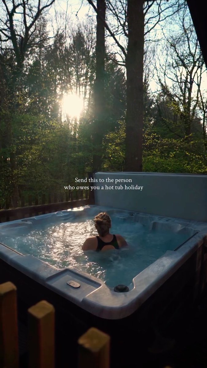 A person relaxes in a hot tub surrounded by trees with sunlight filtering through, featuring overlaid text: 'Send this to the person who owes you a hot tub holiday'.
