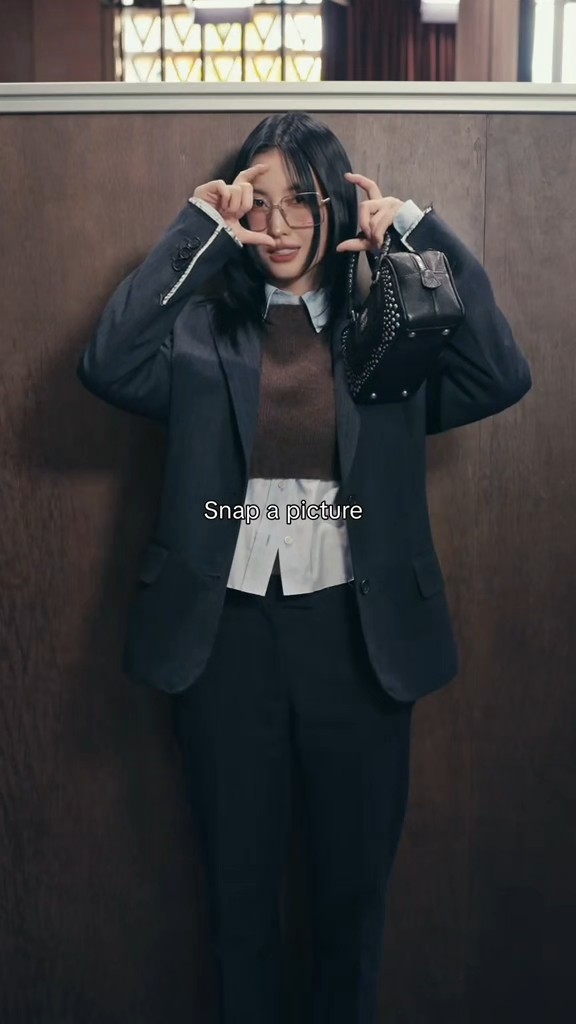 A young woman wearing glasses, a grey blazer, and a small black bag poses playfully, with the text 'Snap a picture' overlaid on the image.