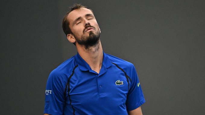 A bearded tennis player in a blue Lacoste polo shirt stands with his eyes closed and head tilted back in apparent frustration. The image, paired with a post about Daniil Medvedev's China Open disqualification, likely shows Medvedev reacting to the incident that prompted calls for rule changes in tennis.