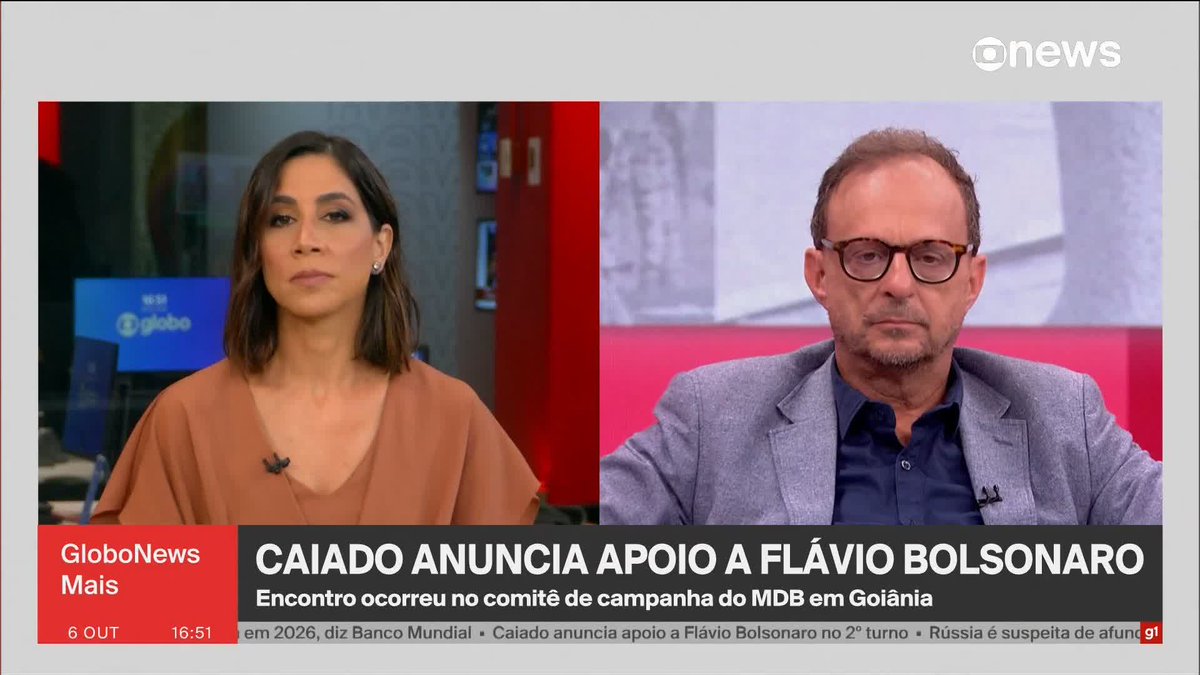 A split-screen broadcast from GloboNews' "GloboNews Mais" program shows a female anchor on the left and a male commentator wearing glasses and a gray blazer on the right, with the headline "CAIADO ANUNCIA APOIO A FLÁVIO BOLSONARO" displayed at the bottom, indicating coverage of Ronaldo Caiado's announcement supporting Flávio Bolsonaro at the MDB campaign office in Goiânia on October 6 at 4:51 PM.