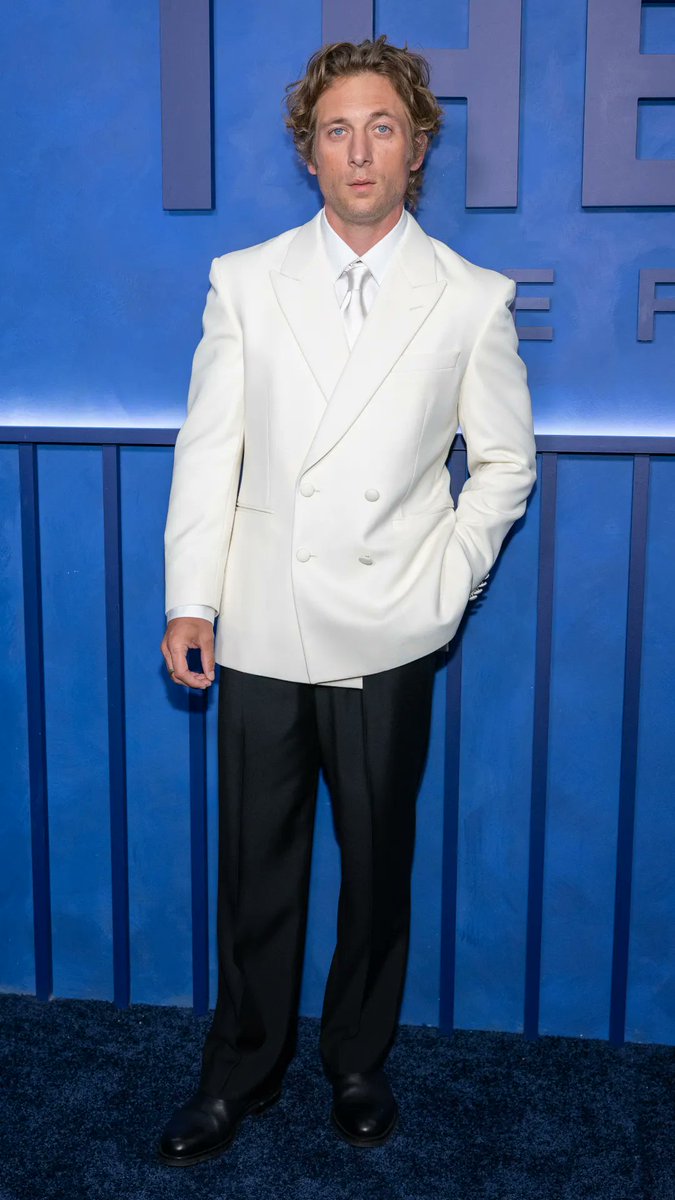 Jeremy Allen White poses on the blue carpet at the premiere of "The Social Reckoning," wearing a white double-breasted blazer with a matching tie and black trousers. The film's title is visible in large lettering on the backdrop behind him, tying directly to the post about his role as a journalist investigating Facebook.