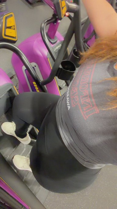 A gym selfie showing a person wearing a black 'BEYOND YOUR LIMITS' workout shirt and leggings using a purple exercise machine.