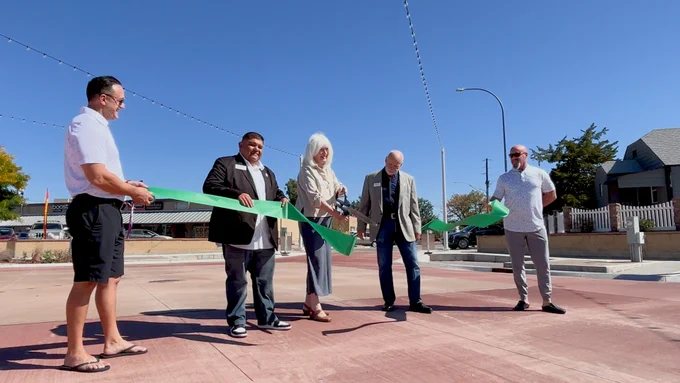 Photo of five people standing behind a piece of green ribbon with the person in the middle holding a pair of scissors that cut it in half