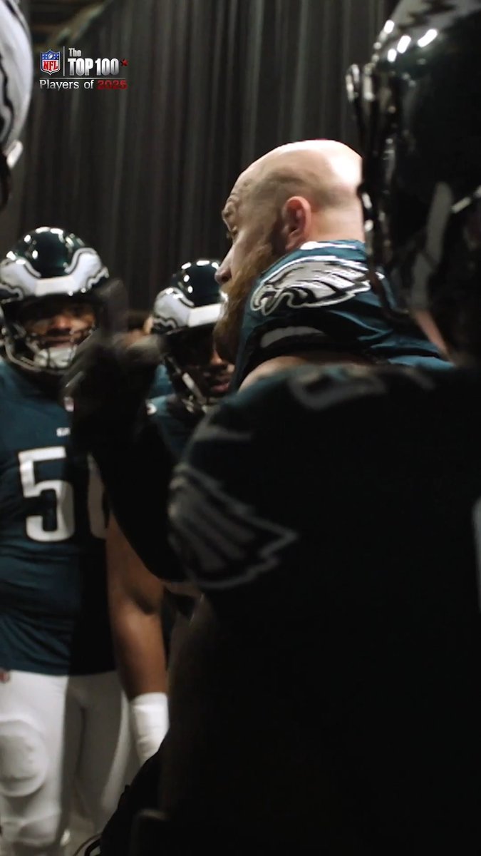 Philadelphia Eagles offensive lineman Lane Johnson, wearing jersey #65, stands in the locker room surrounded by teammates, with an "NFL The Top 100 Players of 2025" logo visible in the upper left corner, celebrating his recognition as one of the league's top players.