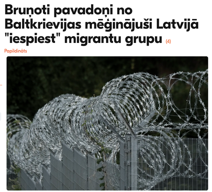 A news headline in Latvian reads "Bruņoti pavadoņi no Baltkrievijas mēģinājuši Latvijā 'iespiest' migrantu grupu," with a "(4)" indicating updates and a "Papildināts" (updated) label, displayed above a photograph of concertina (razor) wire coiled along a border fence. The image visually relates to the accompanying report about armed Belarusian men attempting to force a group of approximately 20 migrants across the Latvia border while threatening troops.