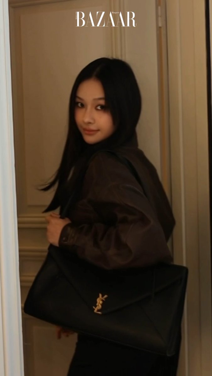 Milk Pansa poses in a dark leather jacket carrying a black Saint Laurent envelope clutch, showcasing the elegant YSL x Milk Pansa pairing for the Saint Laurent SS27 collection at PFW.