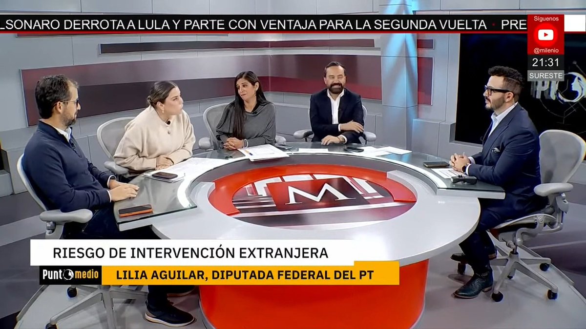 A Spanish-language news panel discussion on the show 'Punto Medio' on the TMI channel, featuring five people around a circular desk with the TM logo, discussing 'RIESGO DE INTERVENCIÓN EXTRANJERA' with guest 'LILIA AGUILAR, DIPUTADA FEDERAL DEL PT,' and a ticker mentioning a runoff election ('SEGUNDA VUELTA') involving Lula.