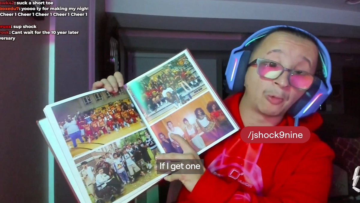 A woman wearing glasses, a red hoodie, and a blue gaming headset holds up an open photo album while live streaming, with the handle '/jshock9nine' and chat messages visible on screen.