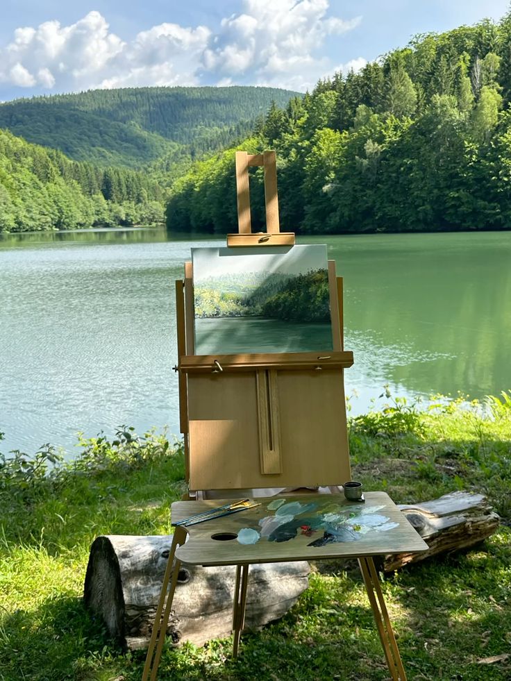 greenvibe's tweet photo. An easel by the lake holds a painting of the same view. https://t.co/5iKafTK78e