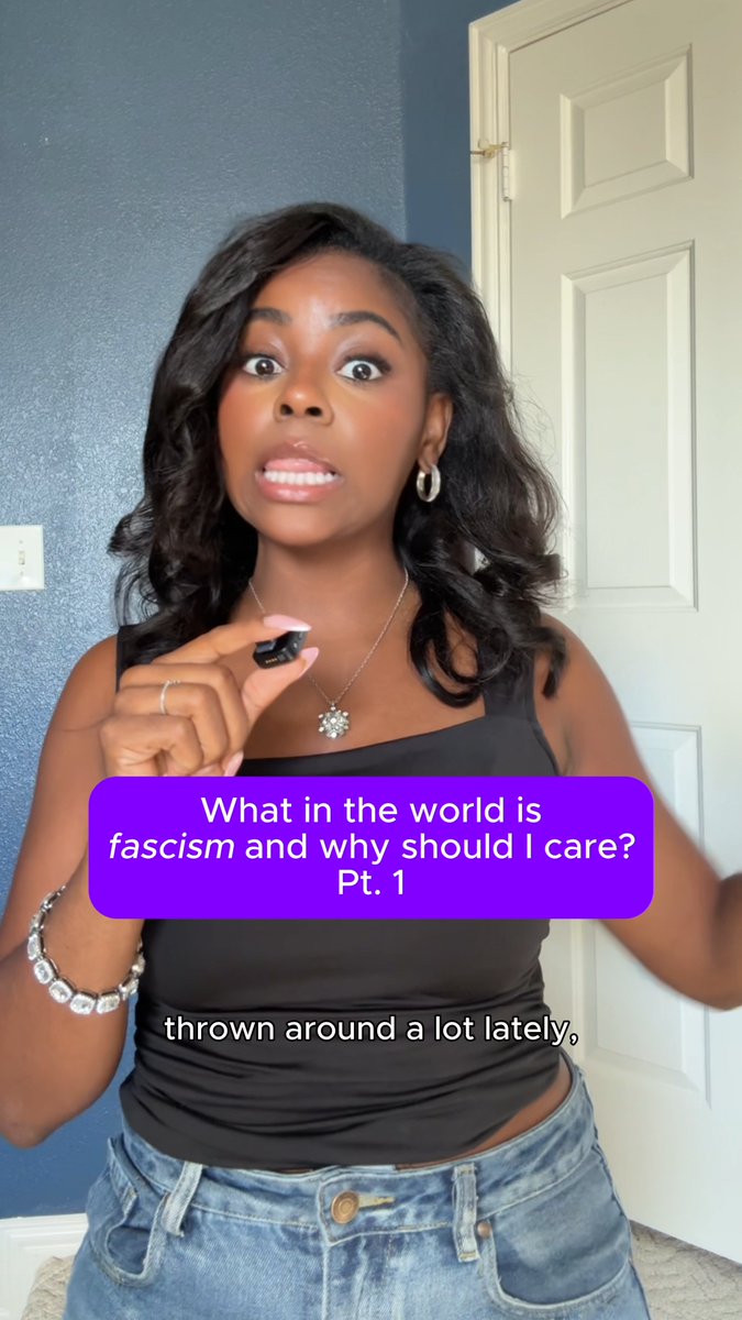 A woman in a black top stands indoors with a purple text overlay reading 'What in the world is fascism and why should I care? Pt. 1' and subtitles stating 'thrown around a lot lately,'
