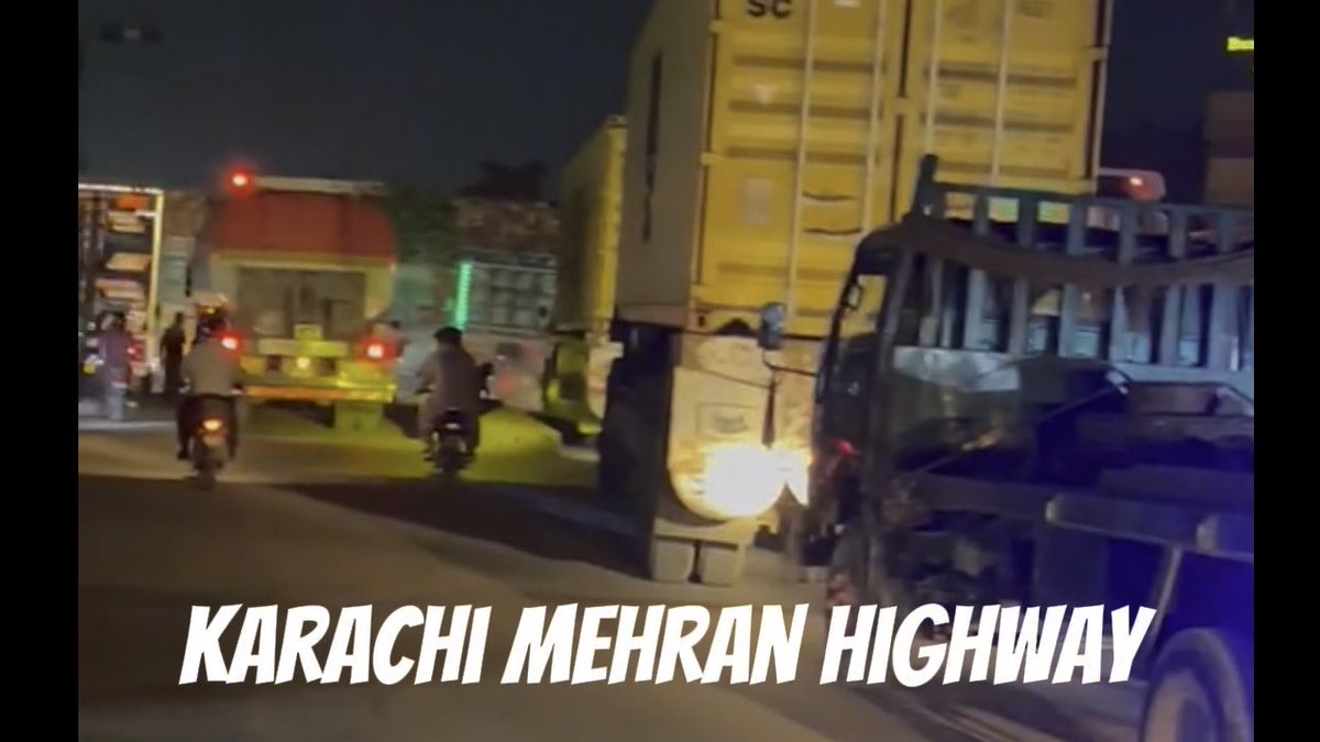 A bustling highway scene at night showing trucks, motorcycles, and pedestrians with the text 'KARACHI MEHRAN HIGHWAY' overlaid.