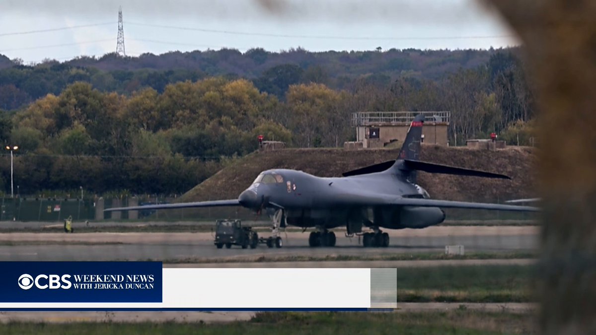 A U.S. Air Force B-1B Lancer bomber is towed on the tarmac at an air base, with the "CBS Weekend News with Jericka Duncan" logo displayed. The image relates to the breaking news of the U.S. withdrawing its twelve B-1 bombers from a British air base due to threats of an Iran-backed attack.