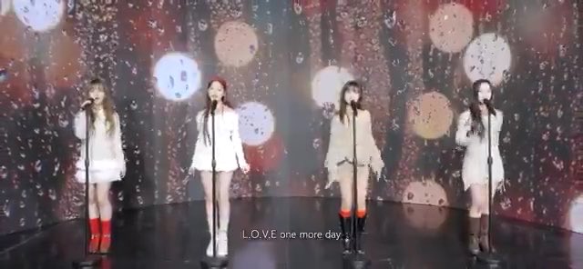 Four female performers in matching white dresses and red boots singing on a stage with a galaxy-themed backdrop displaying the text 'L.O.V.E one more day'.
