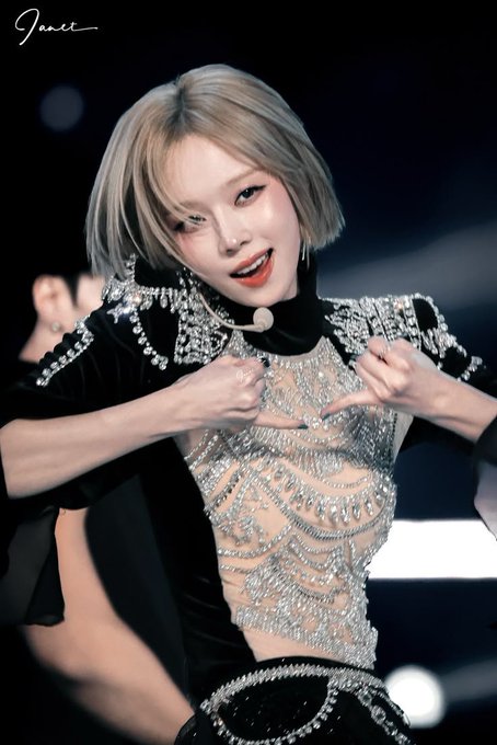 Winter, a member of the K-pop group aespa, performs on stage with short blonde hair, red lipstick, and a sparkling black outfit, forming a heart shape with her hands. The word 'Great' is written in the top left corner.
