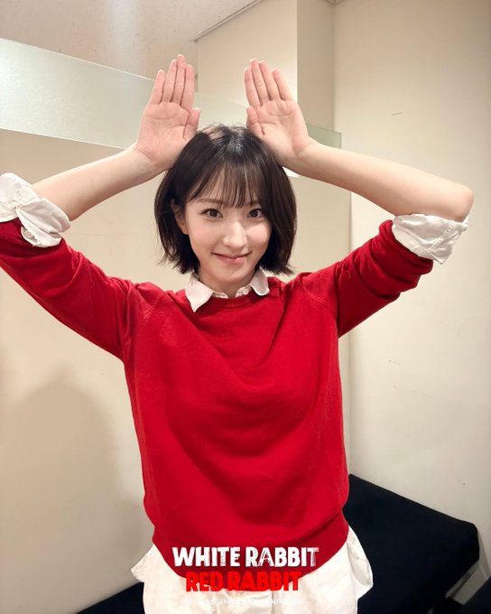 A young woman in a red sweater over a white collared shirt posing with her hands up like rabbit ears, captioned 'WHITE RABBIT / RED RABBIT'.
