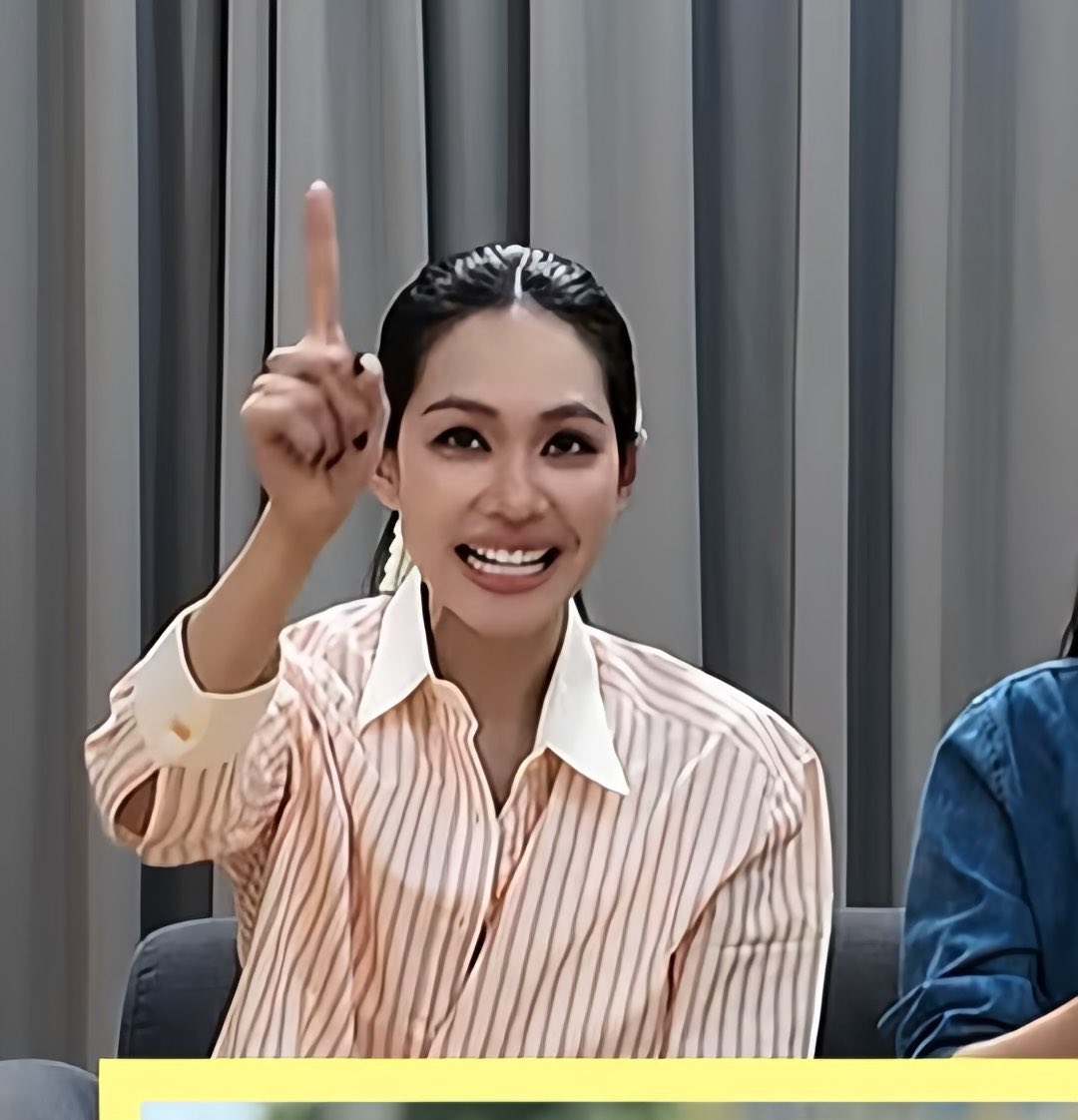 Woman in a peach striped shirt smiling broadly and pointing upward.